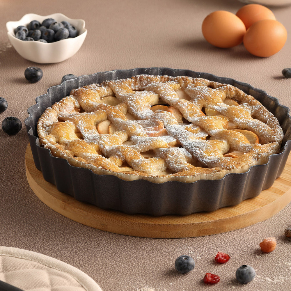 The Zyliss Non-Stick Tart Pan is round and black with fluted edges, a flat bottom, and a removable base—ideal for baking tarts or quiches. The empty pan is displayed on a light background.