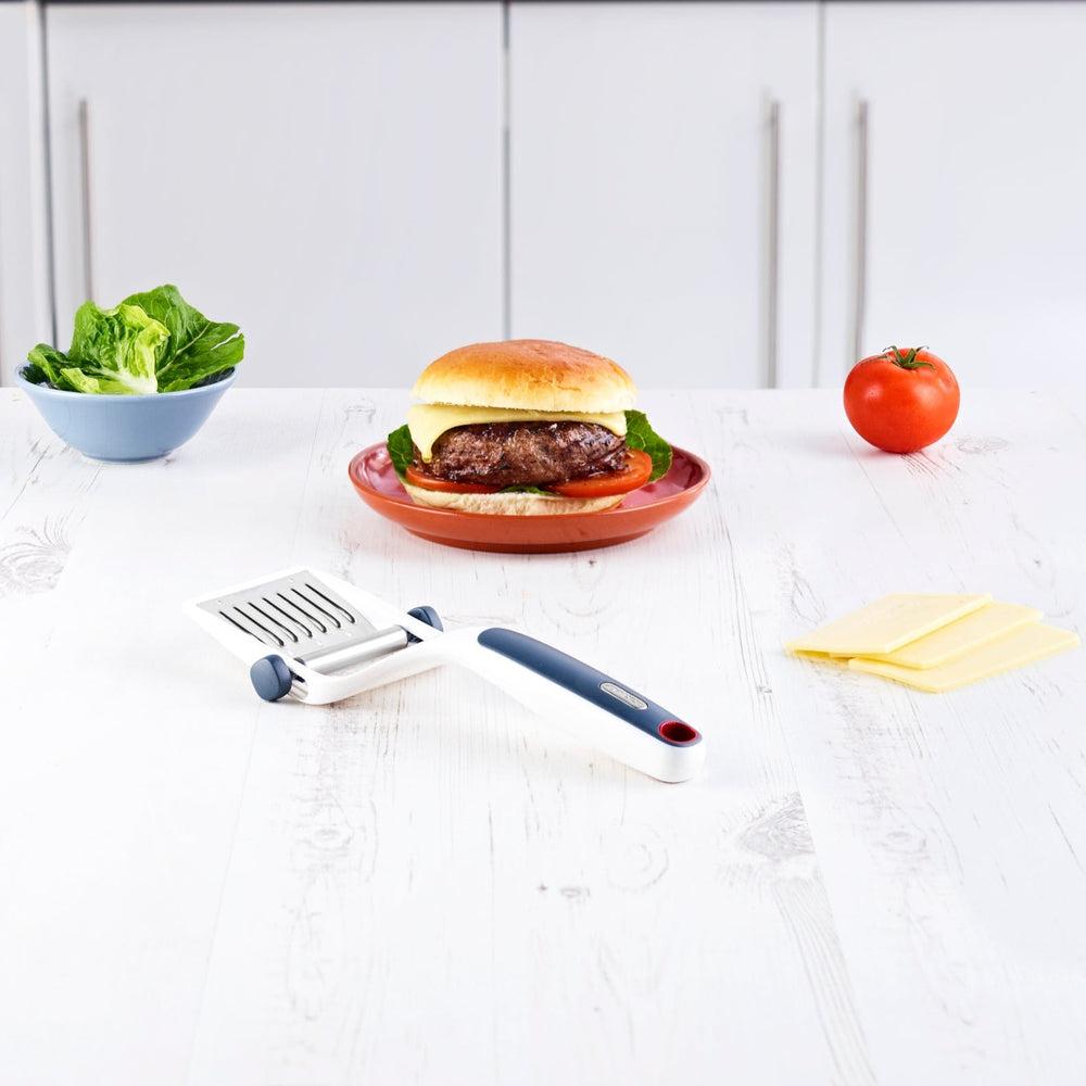 The Zyliss Dial & Slice Cheese Slicer features a white plastic body, gray and red ergonomic handle, and an adjustable blade for slicing cheese to your preferred thickness. 