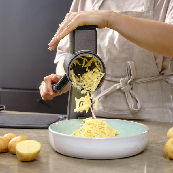 Person using a potato ricer to transfer cooked potatoes into a bowl on a kitchen counter.