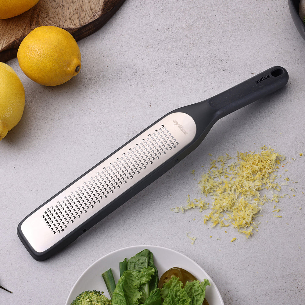 The Zyliss Rasp Grater is a long, rectangular foot file with a gray handle and textured metal surface for removing calluses and dead skin. The handle features a hanging hole for easy storage. 