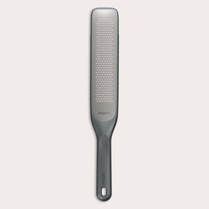 The Zyliss Rasp Grater is a long, rectangular foot file with a gray handle and textured metal surface for removing calluses and dead skin. The handle features a hanging hole for easy storage. 