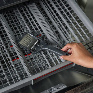 A hand places the Zyliss Utility Cheese Plane on the top rack of a dishwasher, showing that it's dishwasher safe.