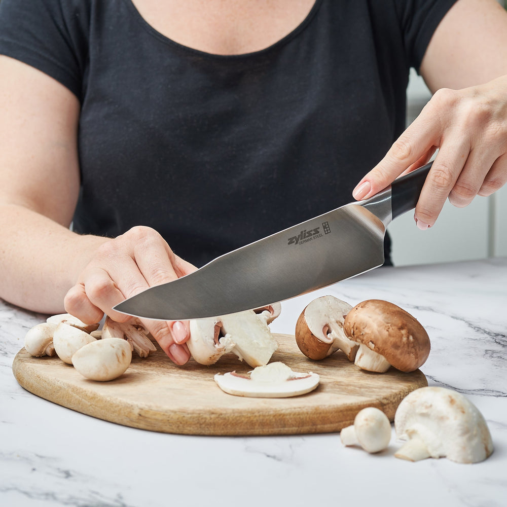 The Zyliss Comfort Pro Chefs Knife 20cm/8, with a German stainless steel blade and a black and silver ergonomic handle, is shown standing vertically on a light, plain background. 