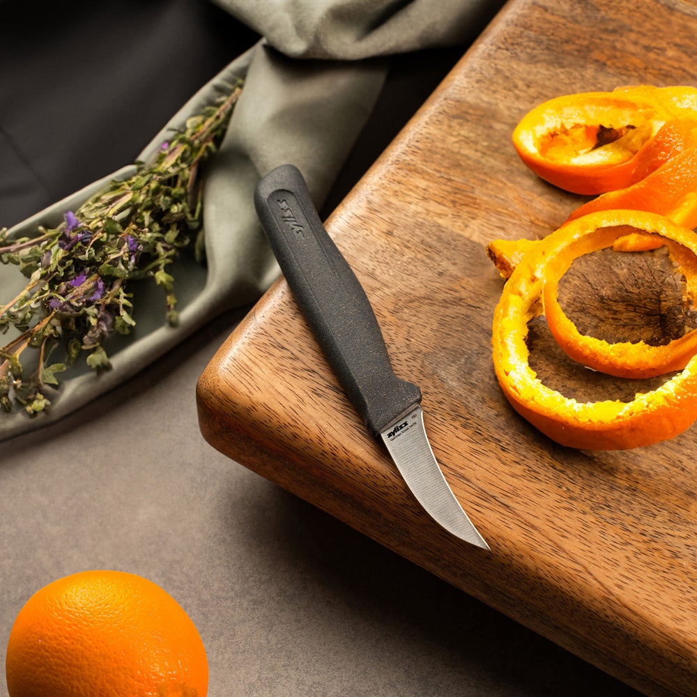 The Zyliss Peeling Knife 6cm (2½) features a curved, sharp stainless steel blade and an ergonomic, eco-friendly wheat straw handle, shown on a plain light background. 