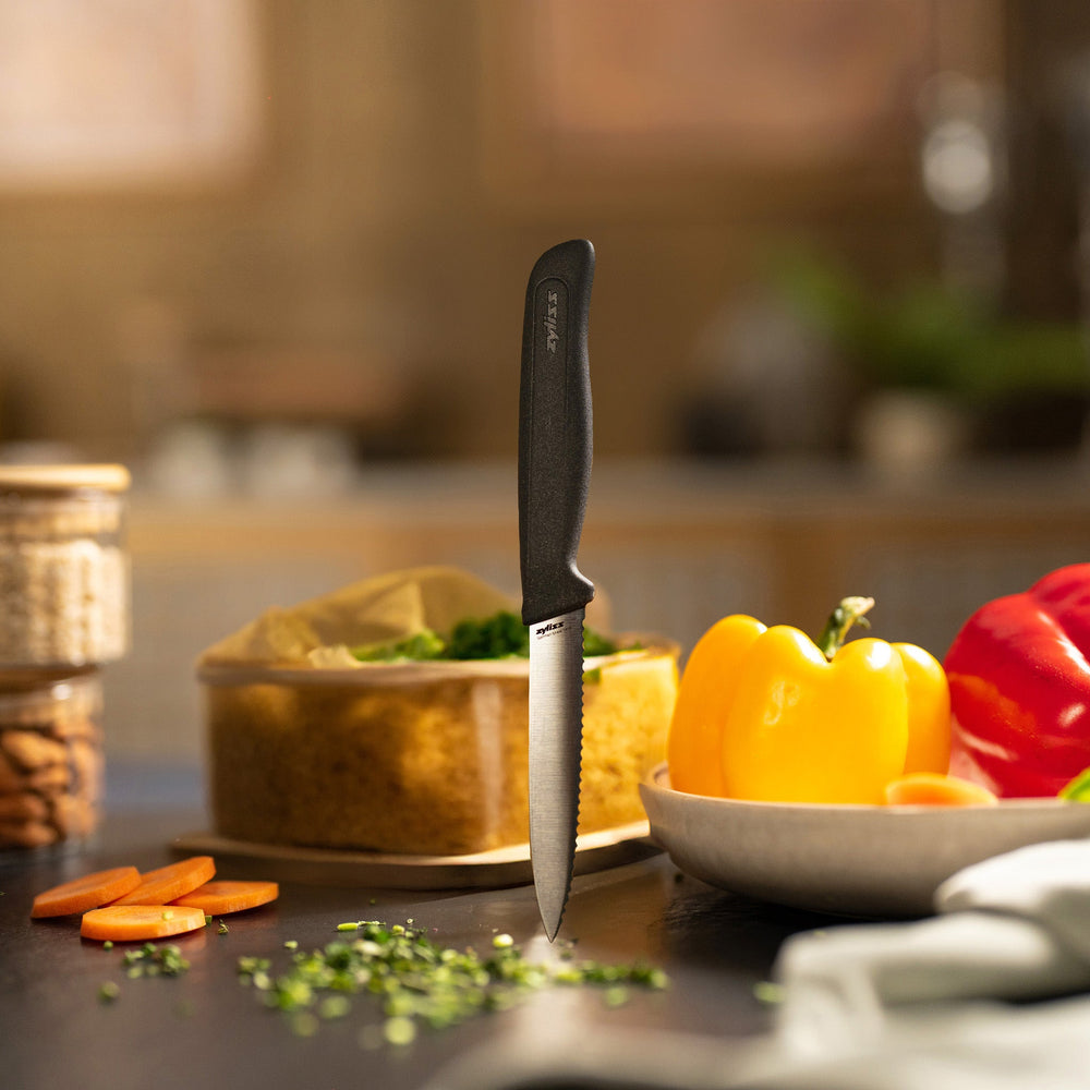 The Zyliss Paring Knife Serrated 10cm / 4, featuring a black ergonomic handle and eco-friendly material, is displayed against a plain white background. 