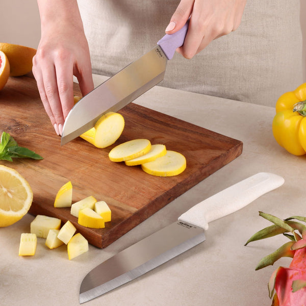 Using the Zyliss Classic 2 Piece Santoku Knife Set, a person slices yellow squash on a wooden cutting board, alongside diced squash, a lemon half, basil, a yellow bell pepper, and the second knife from the set.