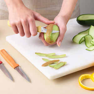 A person uses a small knife from the Zyliss Classic 3 Piece Peeling & Paring Knife Set to peel a kiwi on a white cutting board, with the other knives and cucumber slices nearby.