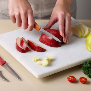 A person slices a red apple on a white cutting board with a paring knife from the Zyliss Classic 3 Piece Peeling & Paring Knife Set, next to corn pieces, halved tomatoes, and the rest of the set.
