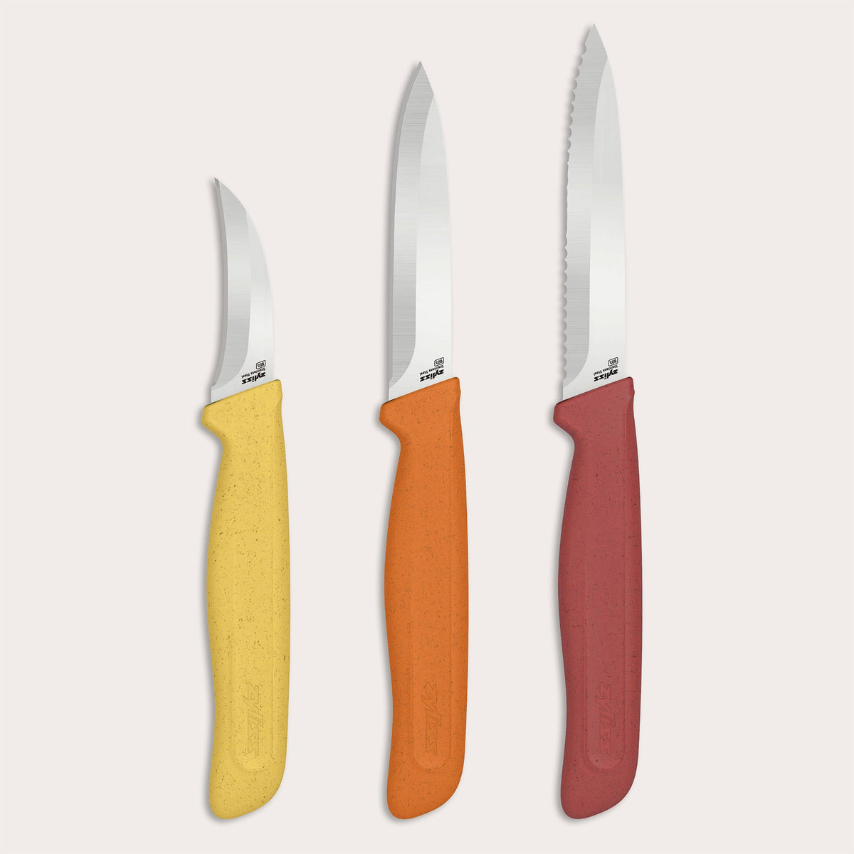 Three knives from the Zyliss Classic 3 Piece Peeling & Paring Knife Set displayed upright against a light background, each with a stainless steel blade and a speckled handle in yellow, orange, or red; the rightmost knife has a serrated blade.