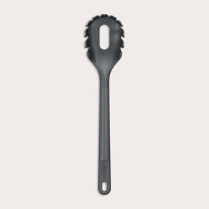 The Zyliss Spaghetti Server is a black, heat-resistant utensil with a long handle and slotted, rounded head featuring prongs for ideal portion control, shown isolated on a light background. 