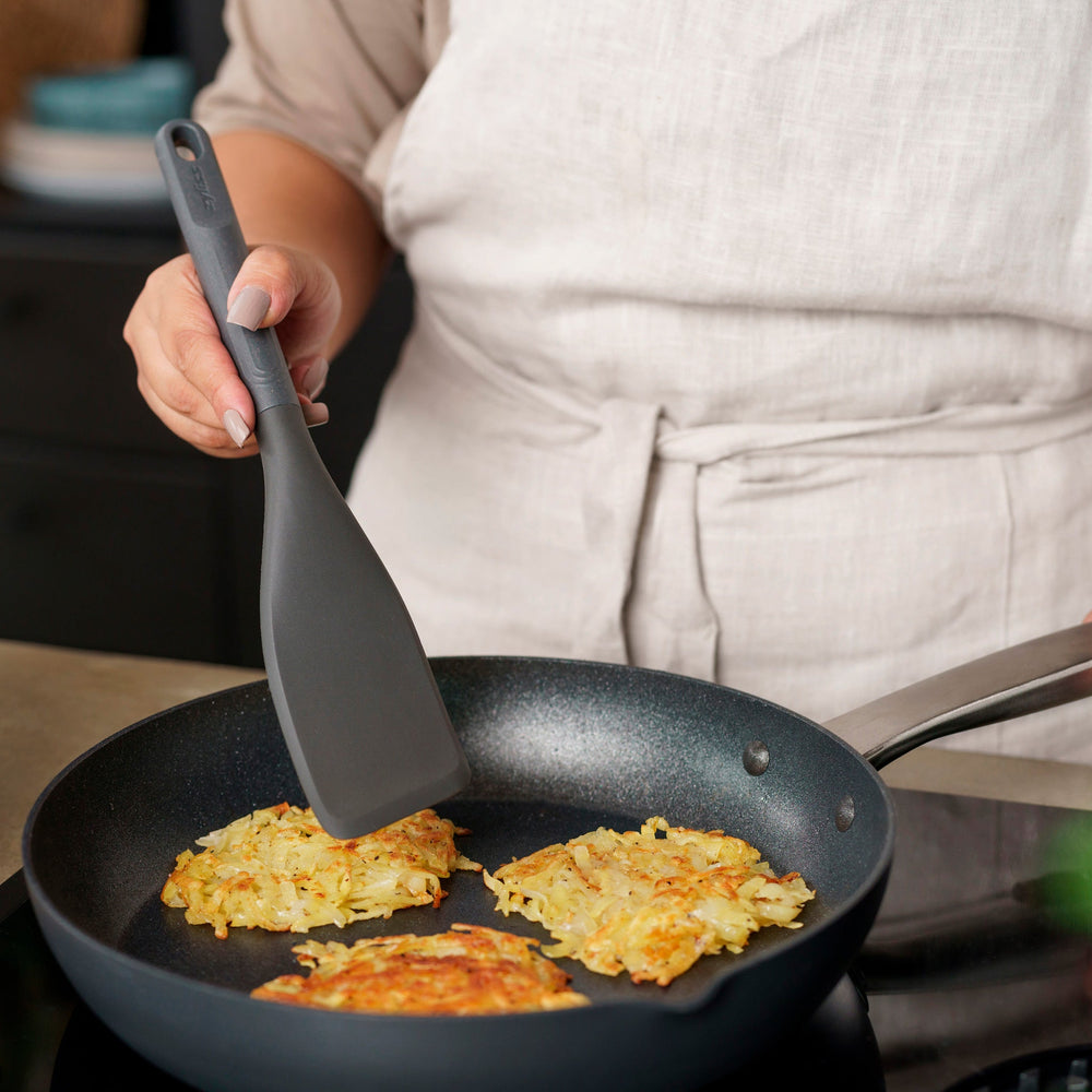 The Zyliss Easy Lift Turner is a gray, heat-resistant silicone utensil with a rectangular, angled head and long handle with hanging hole—perfect for non-stick cookware. Shown on a plain white background. 