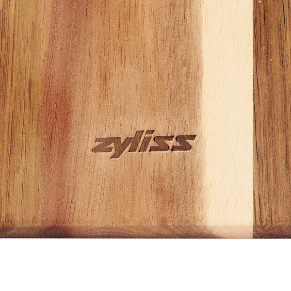 A close-up of the acacia board from the Zyliss Signature 3 Piece Cheese Knife & Acacia Serving Board Set, with zyliss engraved in the center and light and dark brown wood tones.
