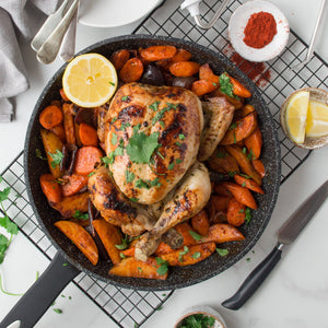 A roasted whole chicken garnished with cilantro sits in the Zyliss Ultimate Non-Stick Frying Pan, surrounded by carrots and potatoes. Lemon halves and paprika highlight its scratch-resistant, quality non-stick surface. #2Pc_Set