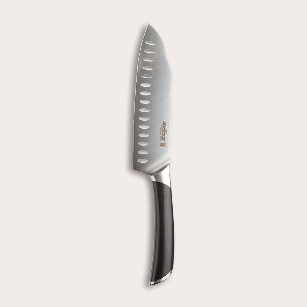 The Zyliss Comfort Pro Santoku Knife 18cm/7 features German stainless steel, a black ergonomic handle, and oval blade indentations, displayed against a light background. 