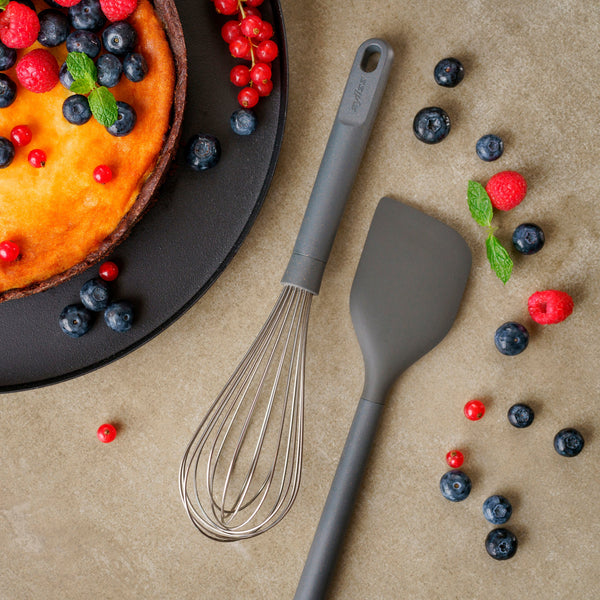 A cheesecake topped with blueberries, red currants, and mint sits beside a Zyliss Balloon Whisk and a gray spatula on the countertop, surrounded by berries—ideal tools for non-stick cookware. #Large